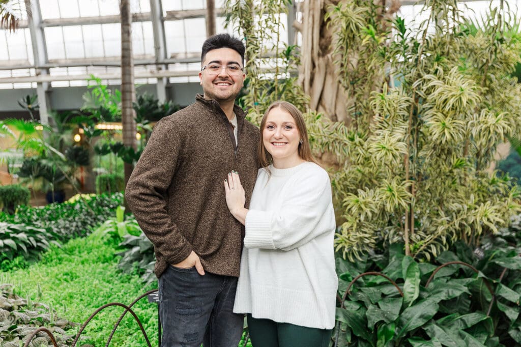 Couple standing side by side with her hand on his chest, smiling at the camera for their engagement session in Chicago