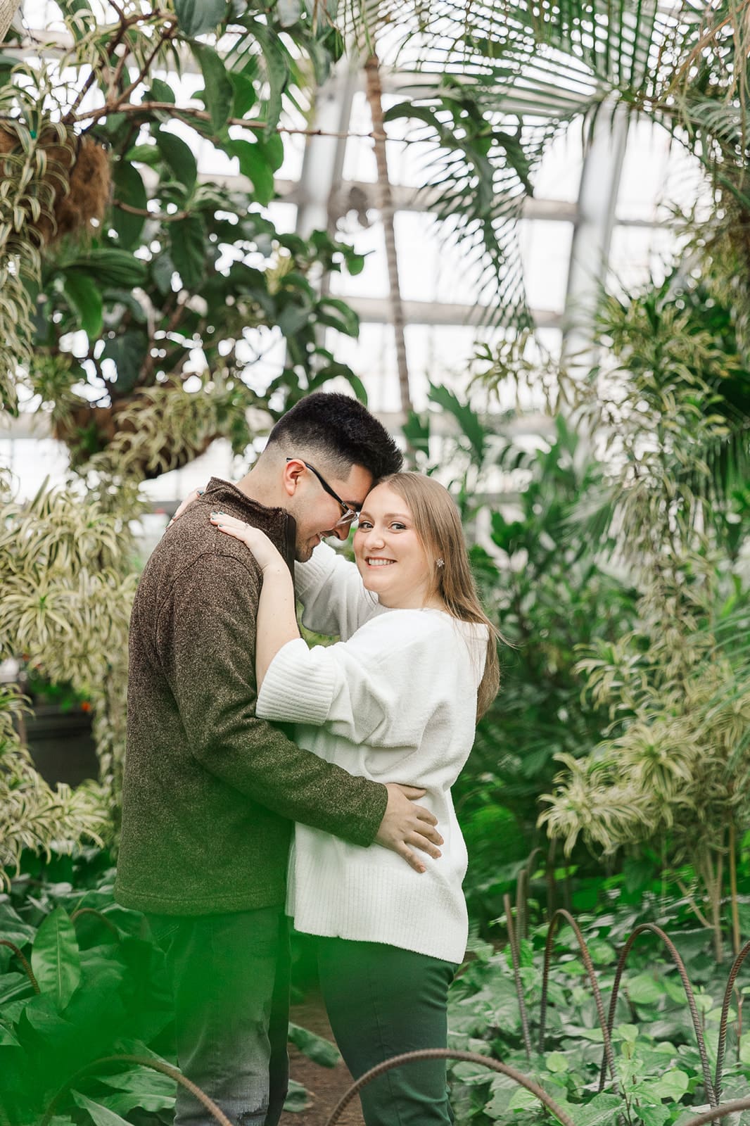 Couple tucked into trees while they smile together during their engagement session at Garfield Park Conservatory.