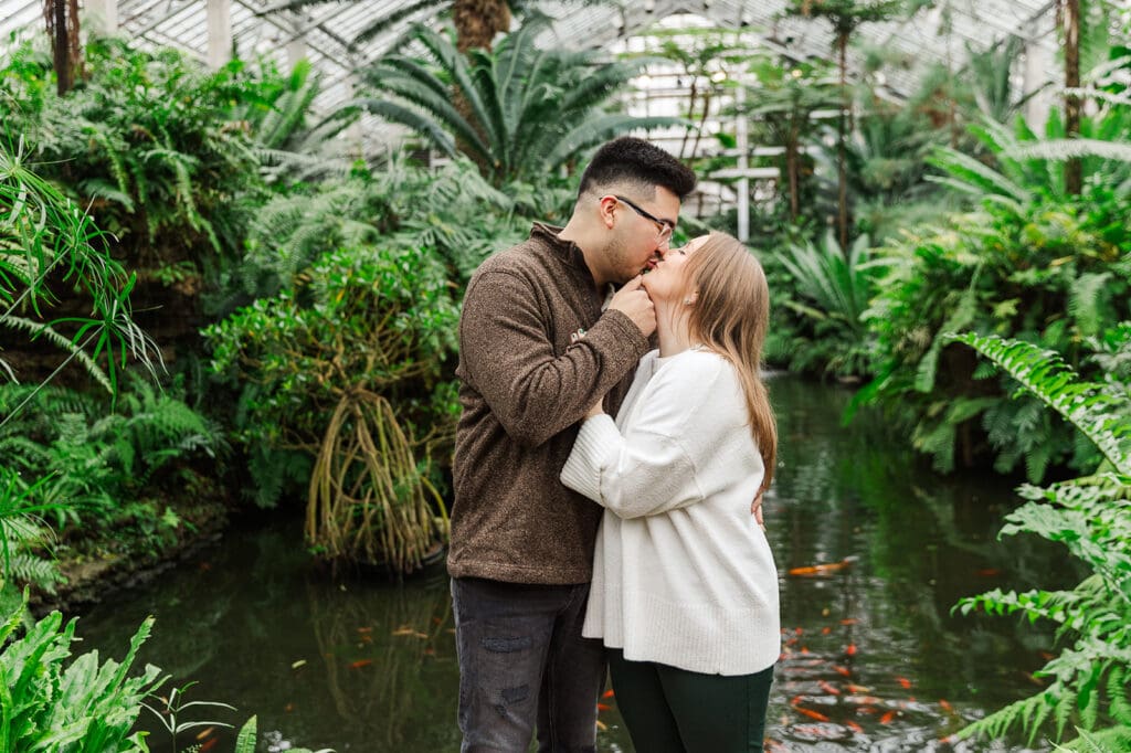 Couple sharing a romantic kiss surrounded by tropical trees during their Chicago engagement session at Garfield Park Conservatory.