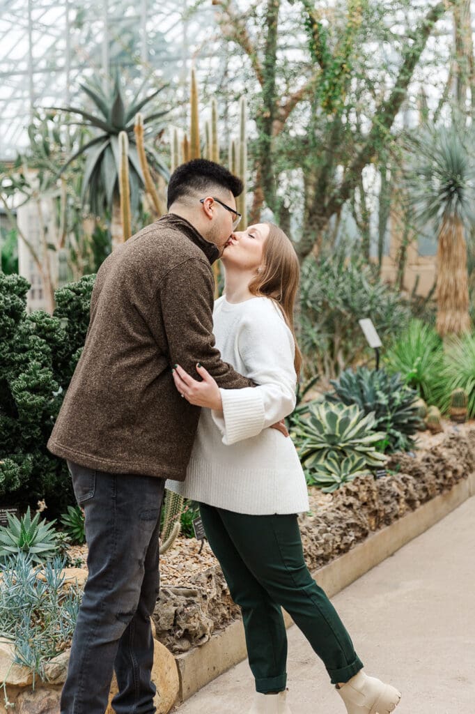 A couple sharing a quick kiss in the cactus room at the Garfield Conservatory in Chicago during their engagement session